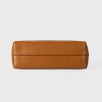 A cognac brown vegan leather baguette shoulder bag with long slim straps and a softly curved top, shown on a white background. Additional product view 5.