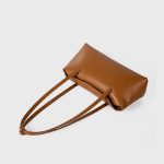 A cognac brown vegan leather baguette shoulder bag with long slim straps and a softly curved top, shown on a white background. Additional product view 6.