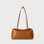 A cognac brown vegan leather baguette shoulder bag with long slim straps and a softly curved top, shown on a white background. Additional product view 7.