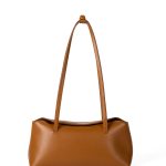 A cognac brown vegan leather baguette shoulder bag with long slim straps and a softly curved top, shown on a white background.