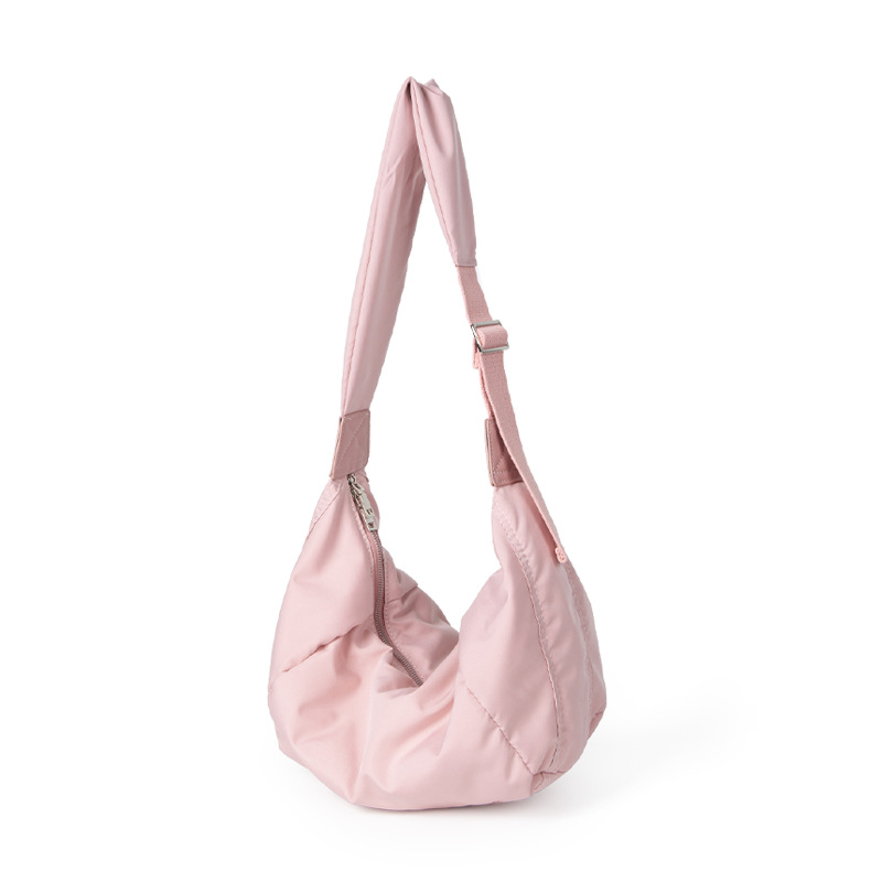 A blush pink padded polyester crescent shoulder bag with a wide adjustable strap and silver zipper, isolated on white.