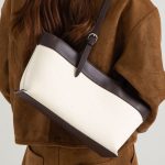 An off-white canvas tote with black vegan leather top trim, base, and adjustable shoulder straps. Additional product view 5.