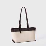 An off-white canvas tote with black vegan leather top trim, base, and adjustable shoulder straps. Additional product view 6.