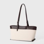 An off-white canvas tote with black vegan leather top trim, base, and adjustable shoulder straps. Additional product view 7.