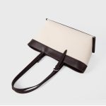 An off-white canvas tote with black vegan leather top trim, base, and adjustable shoulder straps. Additional product view 9.