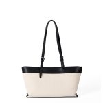 An off-white canvas tote with black vegan leather top trim, base, and adjustable shoulder straps.