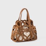 A black laser-cut vegan leather cage tote with a cream drawstring inner pouch and two matching top handles. Additional product view 5.