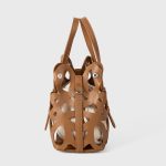 A black laser-cut vegan leather cage tote with a cream drawstring inner pouch and two matching top handles. Additional product view 6.