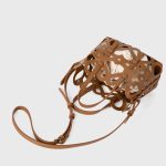 A black laser-cut vegan leather cage tote with a cream drawstring inner pouch and two matching top handles. Additional product view 8.