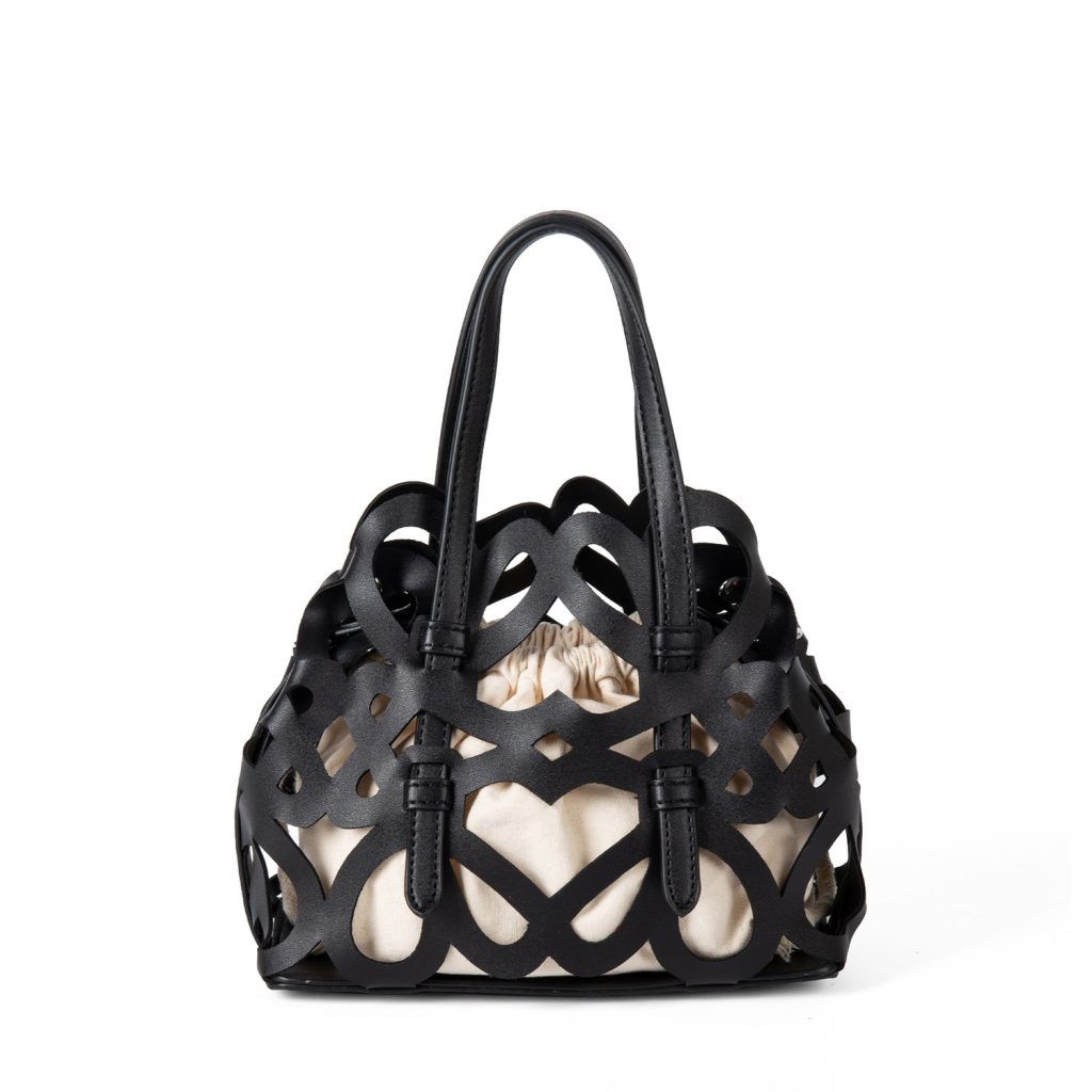 A black laser-cut vegan leather cage tote with a cream drawstring inner pouch and two matching top handles.