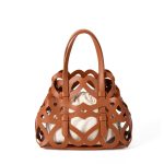 A black laser-cut vegan leather cage tote with a cream drawstring inner pouch and two matching top handles. Additional product view 2.