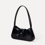 A cognac brown vegan leather baguette shoulder bag with a small front bow on the flap and a slim underarm strap. Additional product view 6.
