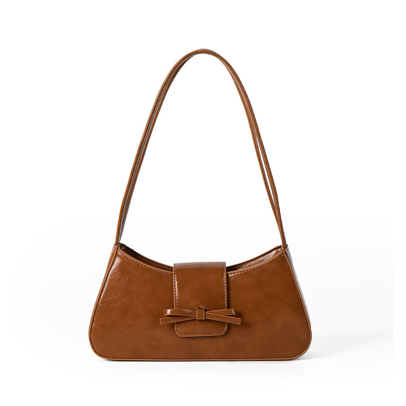 A cognac brown vegan leather baguette shoulder bag with a small front bow on the flap and a slim underarm strap.