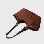 A black faux suede tote with a scooped top, smooth vegan leather trim, and adjustable buckled shoulder straps. Additional product view 6.