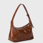 A glossy black crinkled vegan leather crescent underarm bag with a knotted side strap and a silver zipper pull. Additional product view 5.