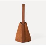 A tall cognac brown faux suede bucket bag with an adjustable vegan leather shoulder strap hanging against a white backdrop. Additional product view 5.