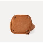 A tall cognac brown faux suede bucket bag with an adjustable vegan leather shoulder strap hanging against a white backdrop. Additional product view 6.