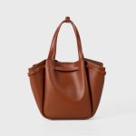 A small black vegan leather bucket bag with dual top handles and a gold-tone buckle strap wrapped around the body. Additional product view 7.