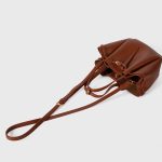A small black vegan leather bucket bag with dual top handles and a gold-tone buckle strap wrapped around the body. Additional product view 9.