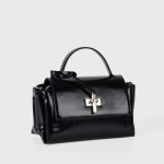 A glossy black structured vegan leather handbag with a thin top handle and a silver cross-bar toggle clasp. Additional product view 5.