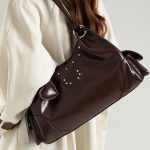 A shiny black vegan leather hobo shoulder bag with a row of silver studs, side flap pockets, and a hanging heart charm. Additional product view 4.