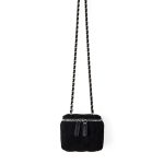 A small black quilted faux suede vanity box bag with dual silver zippers and a chain strap interwoven with black cord.