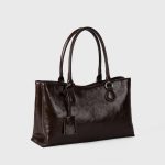 A black vegan leather shoulder tote with a gently scooped top, tubular handles, and a matching hanging leather tag. Additional product view 4.