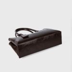 A black vegan leather shoulder tote with a gently scooped top, tubular handles, and a matching hanging leather tag. Additional product view 5.