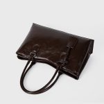 A black vegan leather shoulder tote with a gently scooped top, tubular handles, and a matching hanging leather tag. Additional product view 6.