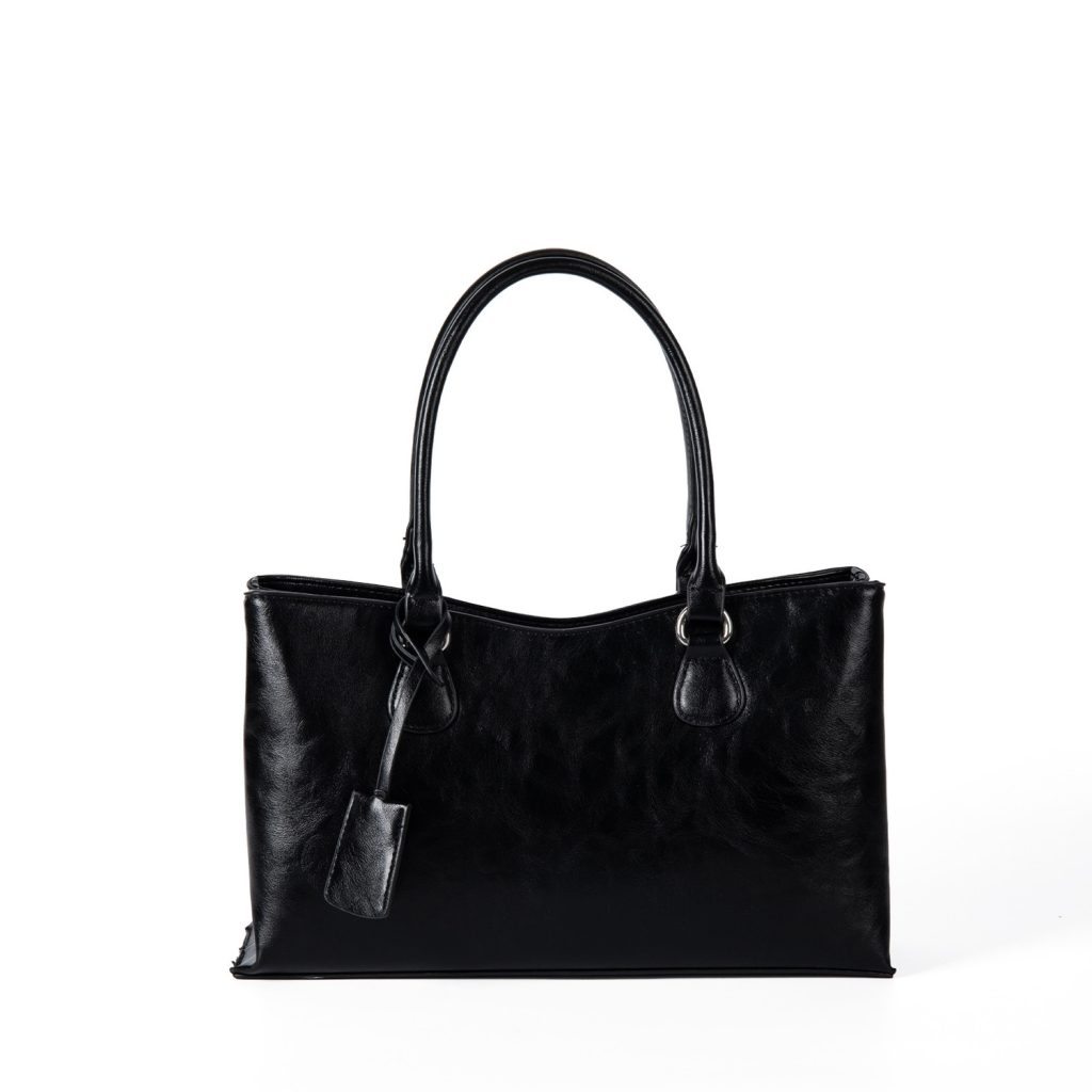 A black vegan leather shoulder tote with a gently scooped top, tubular handles, and a matching hanging leather tag.