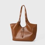 A slouchy black vegan leather tote with integrated shoulder straps and a thin vertical strap finished with a silver buckle. Additional product view 4.