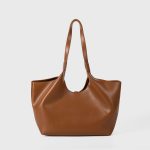 A slouchy black vegan leather tote with integrated shoulder straps and a thin vertical strap finished with a silver buckle. Additional product view 5.