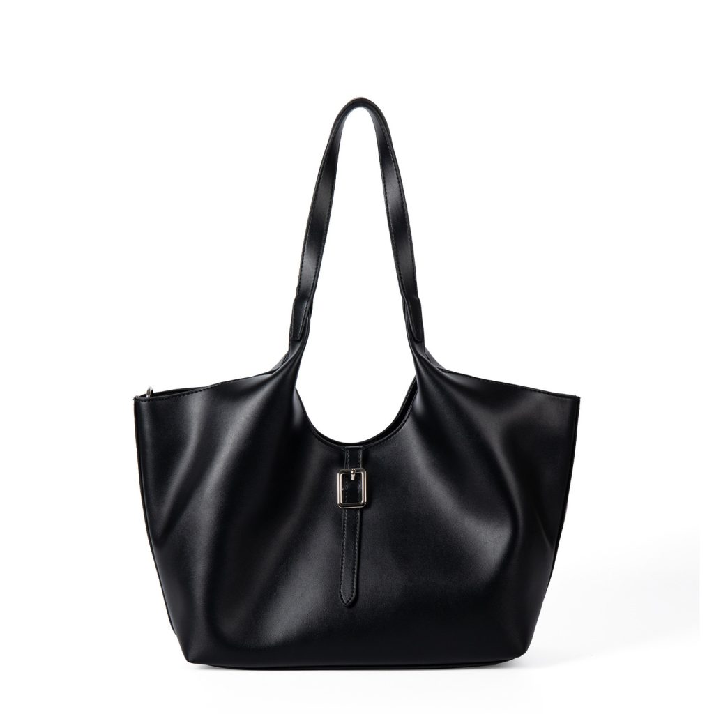 A slouchy black vegan leather tote with integrated shoulder straps and a thin vertical strap finished with a silver buckle.
