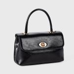 A dark brown glossy vegan leather top-handle flap bag with a gold-tone oval twist-lock centered on the front. Additional product view 7.