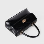 A dark brown glossy vegan leather top-handle flap bag with a gold-tone oval twist-lock centered on the front. Additional product view 10.