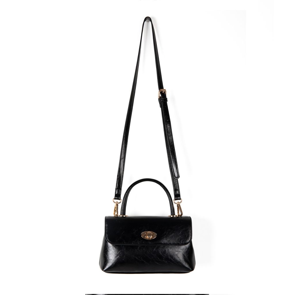 A dark brown glossy vegan leather top-handle flap bag with a gold-tone oval twist-lock centered on the front.