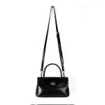 A dark brown glossy vegan leather top-handle flap bag with a gold-tone oval twist-lock centered on the front.