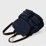 A black nylon backpack with cognac brown vegan leather piping, a top flap over a drawstring, and two lower front pockets. Additional product view 7.