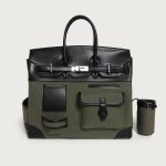 A large black utility tote with mixed canvas and vegan leather panels, multiple cargo pockets, and a silver turn-lock. Additional product view 2.