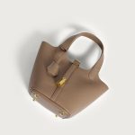A taupe pebbled vegan leather bucket bag with dual top handles, a gold padlock on the center strap, and a matching clochette. Additional product view 5.
