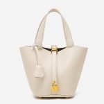 A taupe pebbled vegan leather bucket bag with dual top handles, a gold padlock on the center strap, and a matching clochette. Additional product view 3.