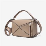 A light beige pebbled vegan leather puzzle bag with diagonal panels, a rolled top handle, and an adjustable shoulder strap. Additional product view 5.
