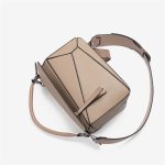 A light beige pebbled vegan leather puzzle bag with diagonal panels, a rolled top handle, and an adjustable shoulder strap.