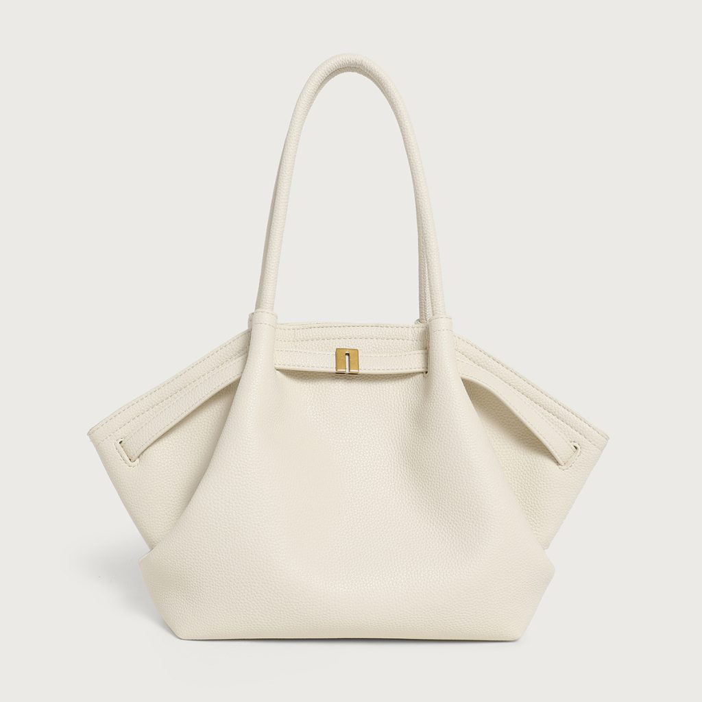A large off-white pebbled vegan leather tote with folded winged sides, slim shoulder straps, and a gold center clasp.