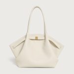 A large off-white pebbled vegan leather tote with folded winged sides, slim shoulder straps, and a gold center clasp.