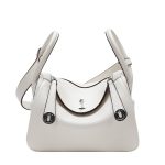 A taupe pebbled vegan leather Lindy bag with side-set handles, a shoulder strap, and silver circular turn-locks. Additional product view 3.