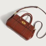 A large cognac brown vegan leather satchel with dual top handles, contrast stitching, and a gold oval turn-lock flap. Additional product view 3.