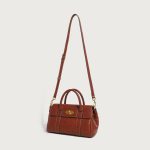 A large cognac brown vegan leather satchel with dual top handles, contrast stitching, and a gold oval turn-lock flap. Additional product view 5.