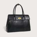 A large cognac brown vegan leather satchel with dual top handles, contrast stitching, and a gold oval turn-lock flap. Additional product view 2.
