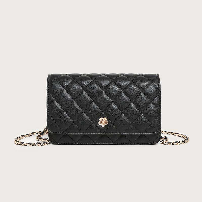 A small black diamond-quilted vegan leather flap bag with a gold flower emblem and a leather-woven gold chain strap.